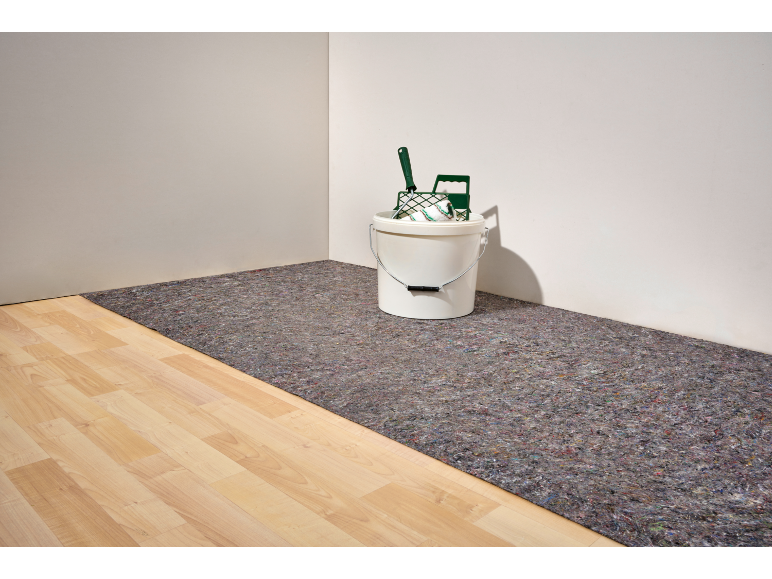 Un seau blanc avec des outils de peinture sur un sous-couche grise sur un plancher de bois clair.