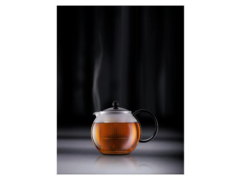 Théière en verre avec du thé infusé et de la vapeur s'élevant sur un fond sombre.