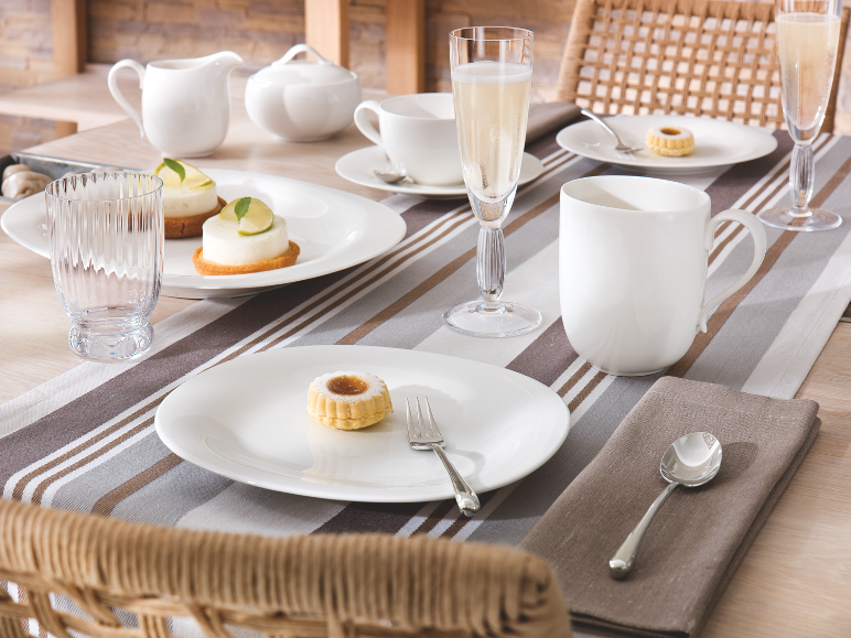 Table dressée avec assiettes, tasses, verres en porcelaine blanche et petites pâtisseries.
