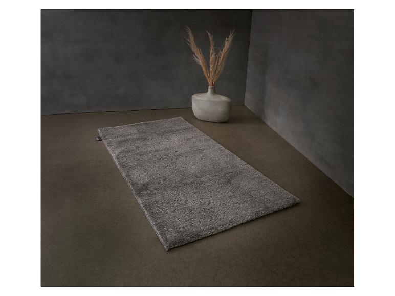 Tapis de bain gris sur sol en béton avec vase et herbe de la pampa.
