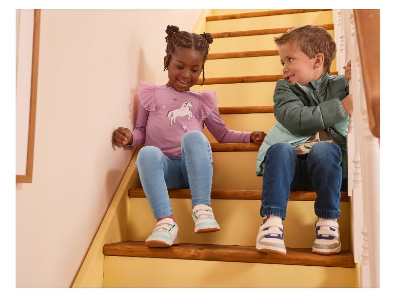Deux enfants assis dans les escaliers, portant un haut à manches longues violet et une veste verte.