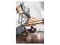 Homme utilisant une perceuse sans fil sous un escalier en bois, avec une lampe de travail à proximité.