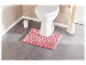 Tapis de salle de bain rose devant des toilettes blanches.