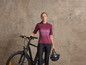 Une femme en tenue de vélo rose avec un vélo noir et un casque.