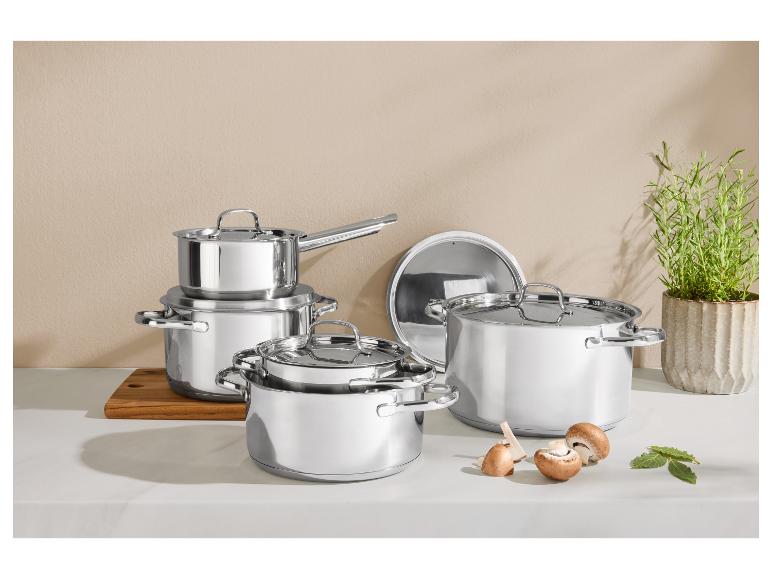Ensemble de casseroles et poêles brillantes en acier inoxydable sur un comptoir de cuisine avec champignons et herbes.