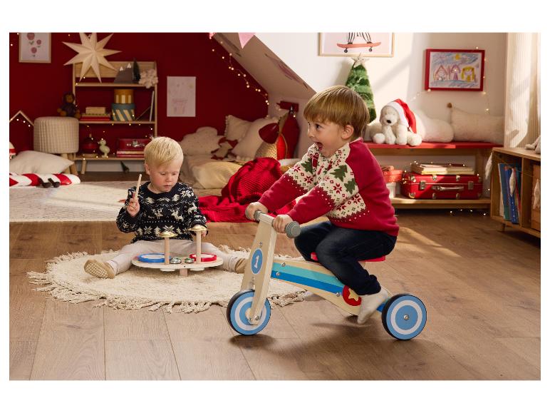 Deux enfants jouent avec des jouets de Noël dans une pièce décorée festivement.