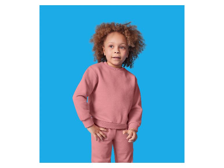 Un jeune enfant aux cheveux bouclés porte un ensemble rose de sweat-shirt et de pantalon de survêtement.