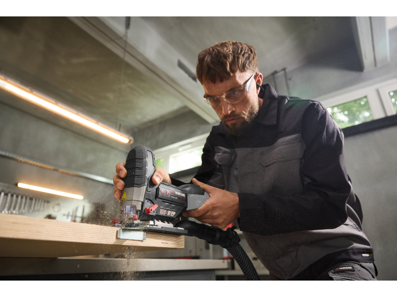 Homme avec lunettes de protection utilisant une scie sauteuse pour couper du bois.