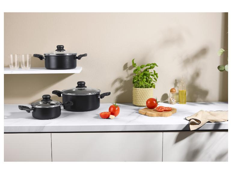 Casseroles noires avec couvercles en verre, tomates fraîches, basilic et accessoires de cuisine.