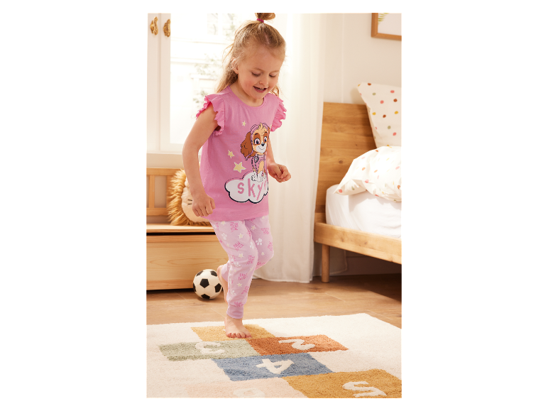 Une fillette en pyjama Pat' Patrouille joue sur un tapis.