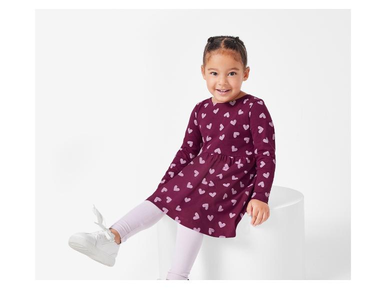 Une fille porte une robe rose à imprimé cœur et des baskets blanches.