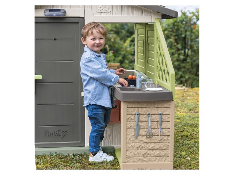 Enfant souriant jouant avec une maisonnette et une cuisine extérieure Smoby.