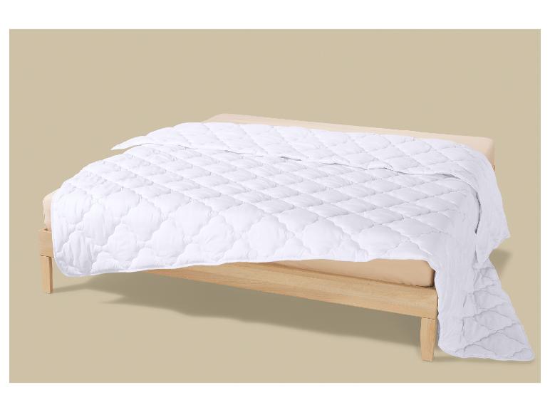 Couverture blanche matelassée sur un lit en bois avec un drap beige.