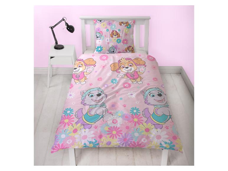 Parure de lit enfant rose à motifs de chiens et de fleurs, sur un lit blanc avec lampe.