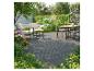 Terrasse extérieure avec revêtement gris foncé, un ensemble de salle à manger et des chaises longues entourées de plantes luxuriantes.