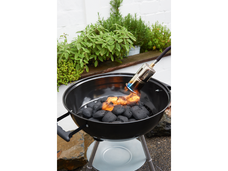 Barbecue au charbon de bois avec allume-feu, entouré de plantes aromatiques.