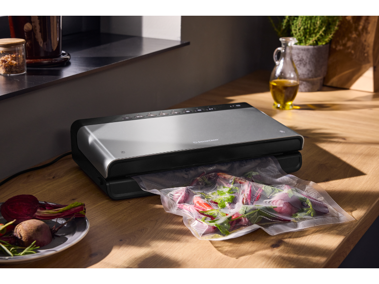 Machine de mise sous vide argentée sur un plan de travail en bois avec un sachet de légumes.