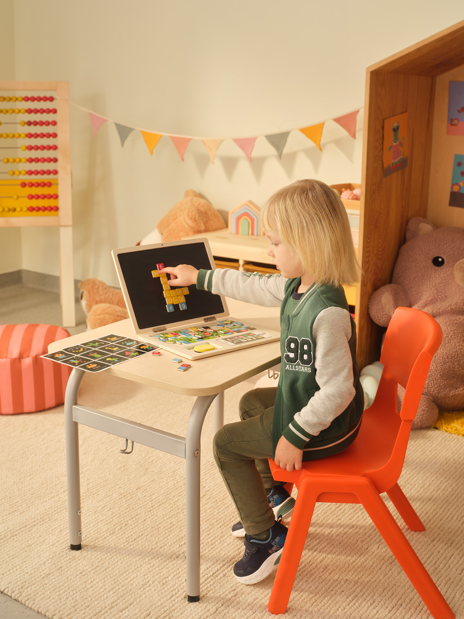 Enfant jouant avec un ordinateur portable en bois et des lettres magnétiques sur un petit bureau.