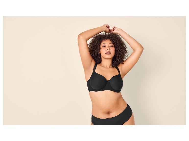 Femme aux cheveux bouclés portant un soutien-gorge et une culotte noirs, bras levés.