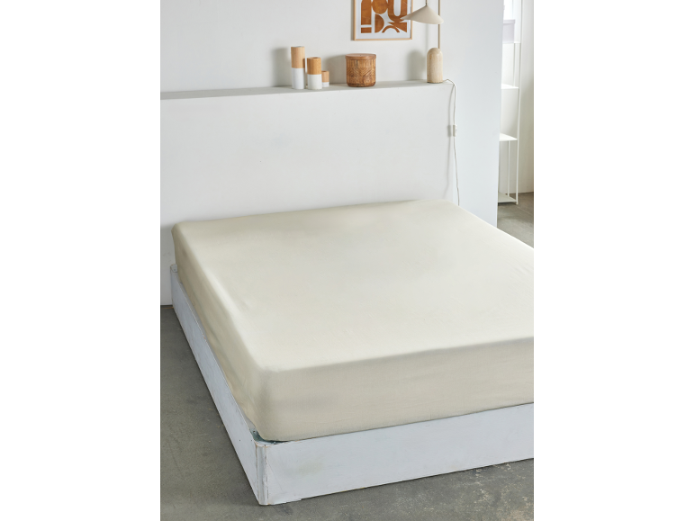 Un lit avec un drap-housse de couleur claire, décor minimaliste sur une étagère au-dessus.