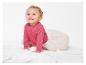 Bébé en pull rose et pantalon beige sur un lit blanc.
