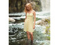 Une femme dans une robe d'été jaune à boutons debout dans une rivière.