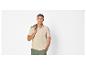 Homme en polo beige et short vert, avec veste verte sur l'épaule.