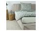 Chambre avec lit, housse de couette grise à motif de feuilles, oreiller et drap blanc.