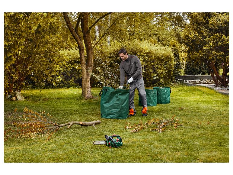 Homme nettoyant des branches dans des sacs de jardin verts, avec une tronçonneuse à côté.