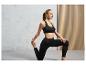 Une femme en soutien-gorge de sport et leggings noirs s'étire.