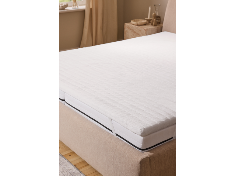 Surmatelas blanc sur un lit dans une chambre aux tons neutres.