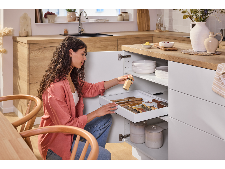 Femme organisant un meuble de cuisine avec tiroir coulissant pour épices et ustensiles.