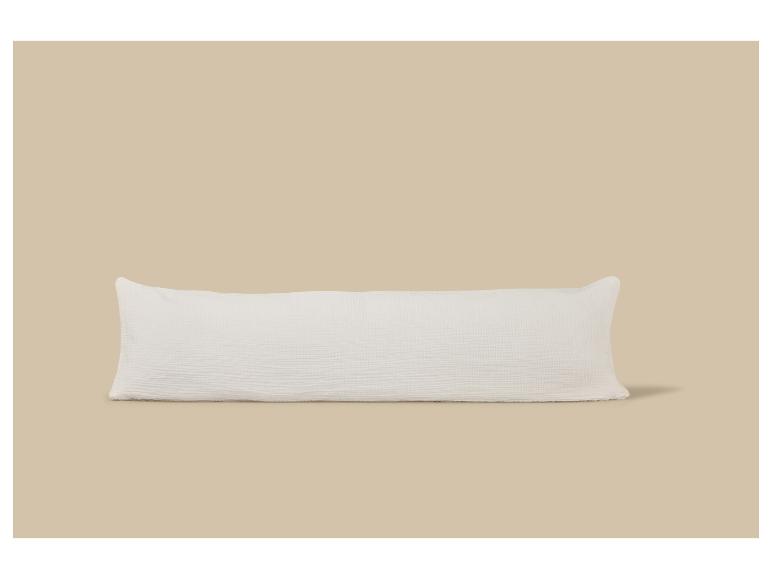 Oreiller de corps texturé blanc sur fond beige.