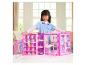 Une fille joue avec une armoire de poupée rose remplie de vêtements et d'accessoires.