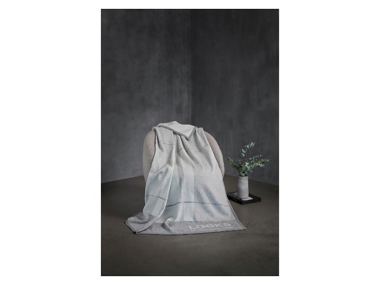 Plaid gris et blanc sur un fauteuil, avec un vase de verdure à côté.