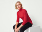 Une femme porte un pull rouge et un pantalon noir.