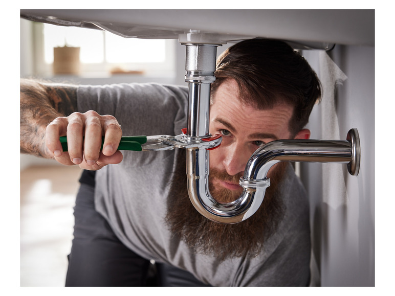 Un plombier travaille sur un évier avec une pince.