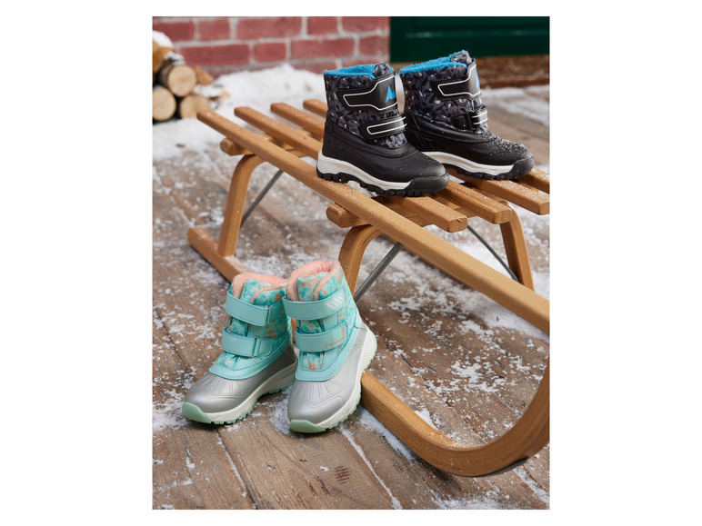 Des bottes d'hiver pour enfants noires et bleues sur un traîneau en bois.