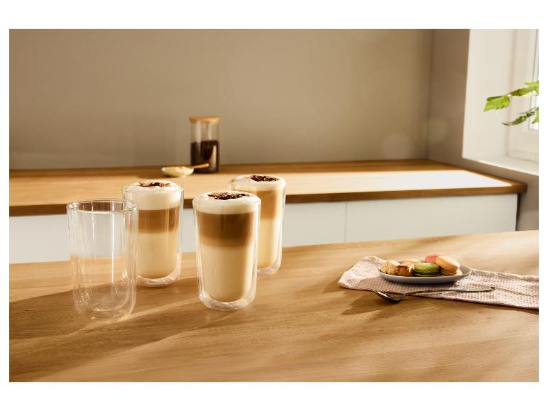 Trois verres de café latte avec mousse et copeaux de chocolat, à côté de macarons et biscuits.