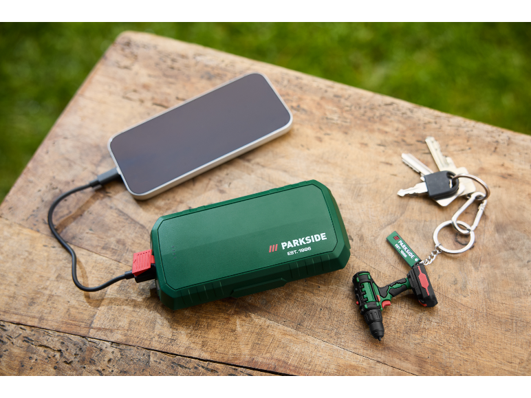 Batterie externe verte chargeant un smartphone, avec des clés et un porte-clés mini-perceuse.