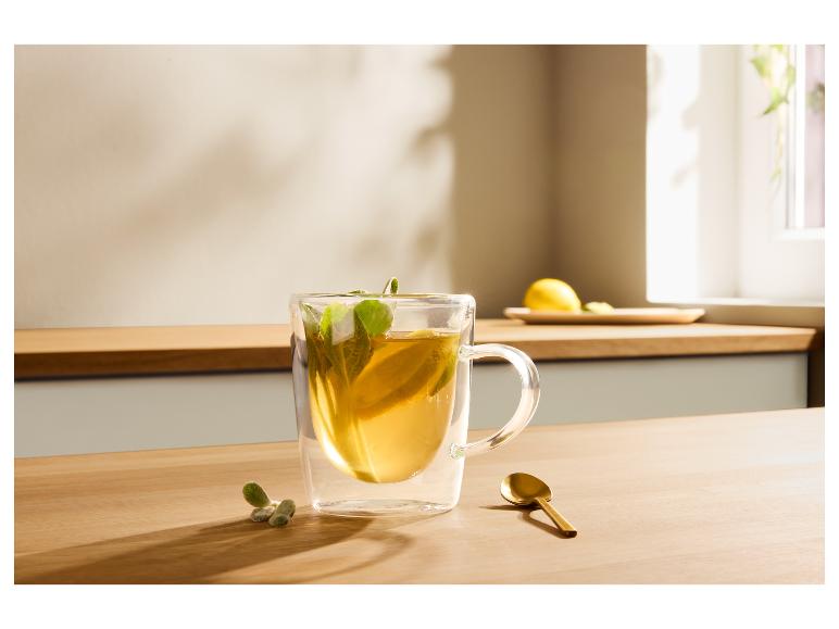Tasse transparente avec thé, citron et menthe sur une table en bois, à côté d'une cuillère dorée.