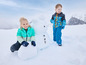Deux enfants en vêtements d'hiver construisent un bonhomme de neige.