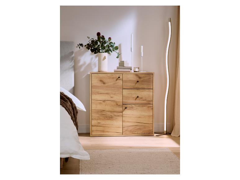 Commode en bois avec tiroirs et portes, décorée d'un vase de fleurs et de bougies, à côté d'un lit.