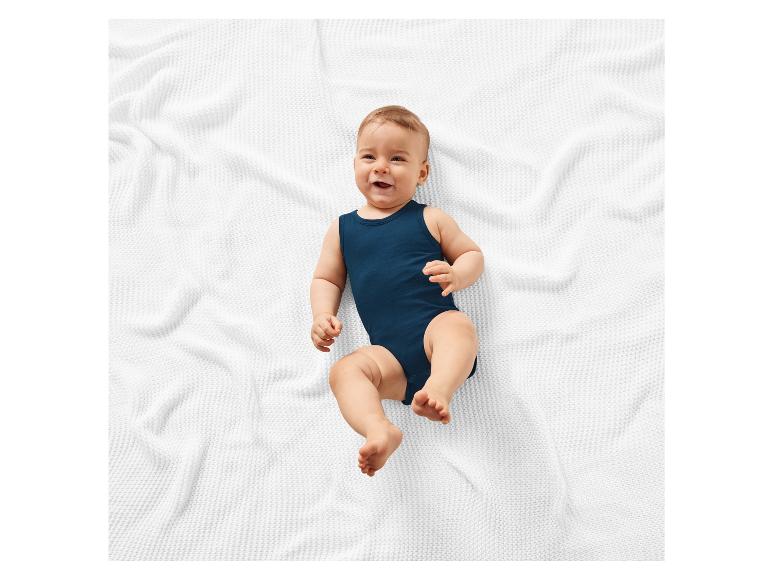 Bébé souriant sur un plaid blanc portant un body bleu marine.