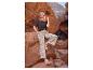 Femme en t-shirt noir et pantalon à motifs, assise sur un rocher dans un canyon.