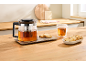 Théière en verre avec thé et biscuits sur un comptoir en bois.