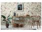 Papier peint floral avec console, plante et photo encadrée dans une pièce chaleureuse.