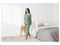 Une femme en pyjama vert à motif de cœurs dans une chambre à coucher.