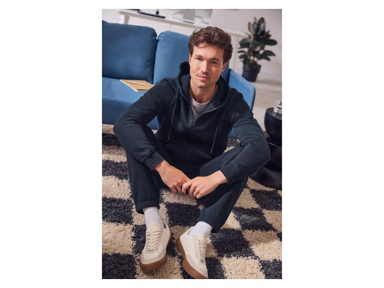 Homme en sweat à capuche bleu foncé et pantalon de survêtement assis sur un tapis.