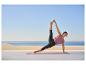 Femme en haut violet et legging noir faisant du yoga sur un tapis sur une terrasse avec vue sur la mer.
